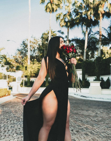 bella mujer en vestido negro enseñando la pierna mientras sostiene un ramo de flores